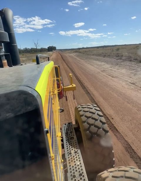 In-cab operator POV on a grader cutting a red-dirt haul road, Blue Mountains NSW