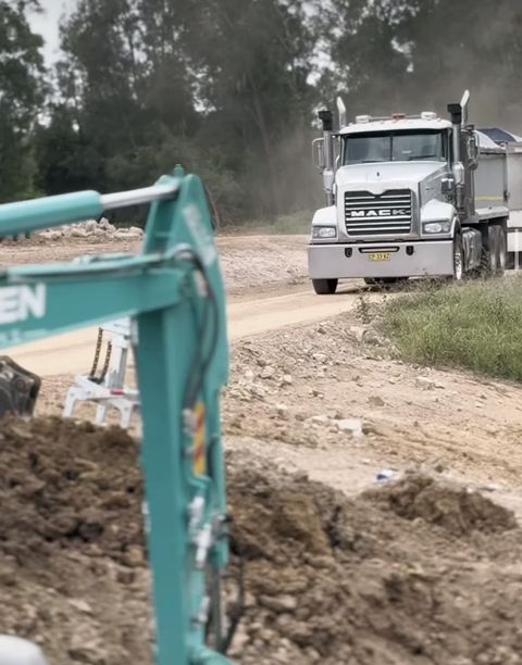 Teal Kobelco 5.5t excavator loading spoil into a white Mack tipper truck, dust rising, Penrith NSW